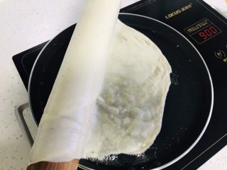 千层酱香饼,拿起饼坯 一头先下入锅中 看到饼皮透明,借助锅铲往右推饼