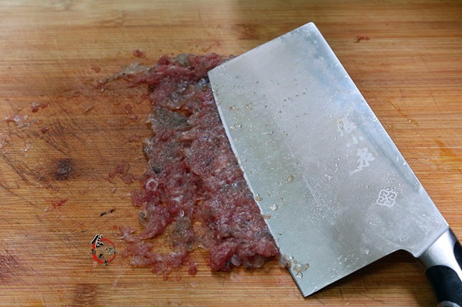 再用刀将剁好的肉碎压烂成肉糜,一手抓住刀柄,一手按在刀面上,稍微