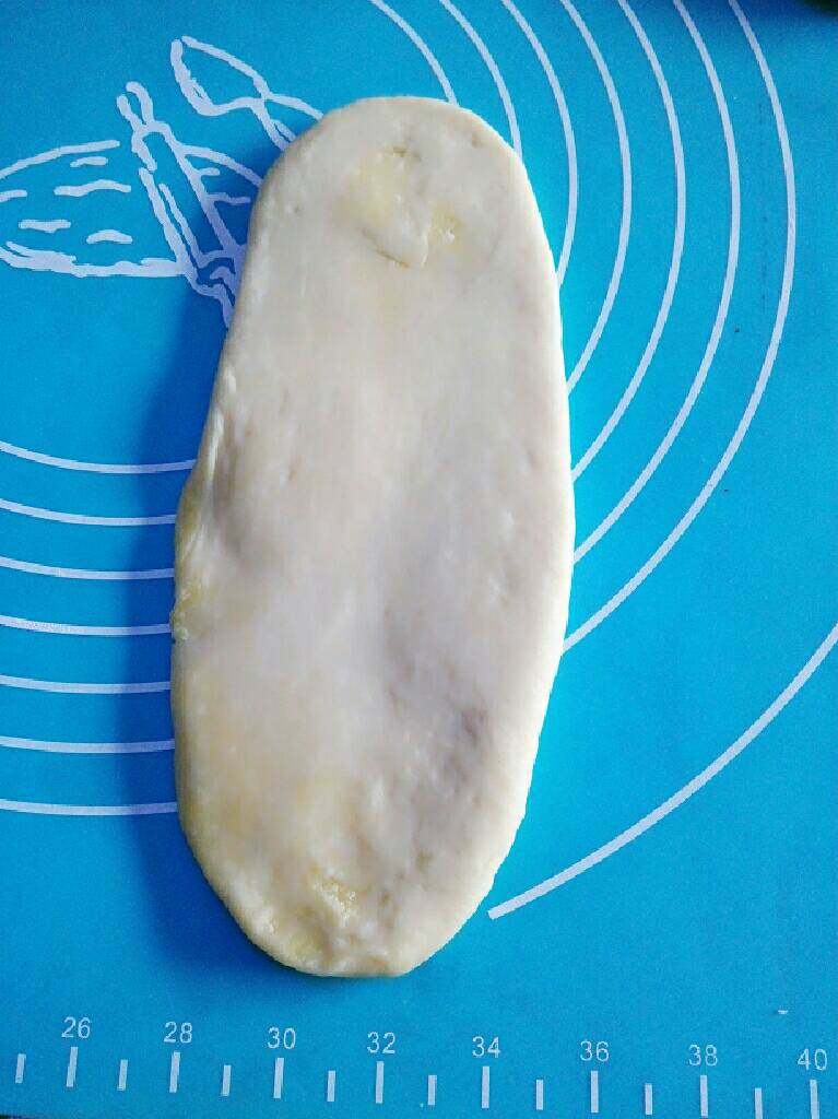 奶香椰蓉面包,用擀面棒将装有椰蓉的面团擀成一个扁的长的椭圆形(须小心地擀，不要将椰蓉馅儿擀出来)。