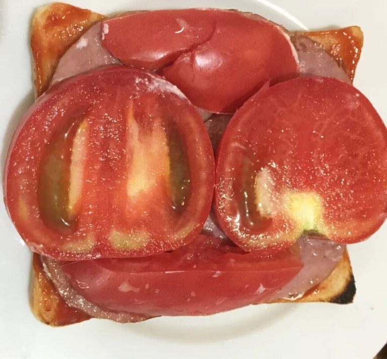 火腿蛋三明治,如图将面包片放在无水无油的盘子里，均匀的涂抹番茄酱加入番茄和煎好的火腿