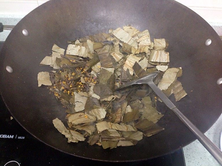 荷熏桂花鸡,取一口无油大锅，倒入荷叶、茶叶和桂花，烘炒至冒烟。