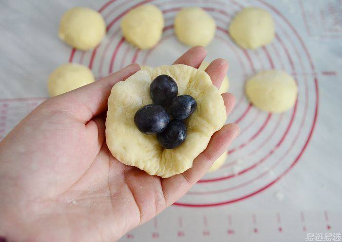 蓝莓泡浆小面包,取一个松驰好的面团，拍扁，四边拍薄一点，中间包上六颗新鲜蓝莓。
