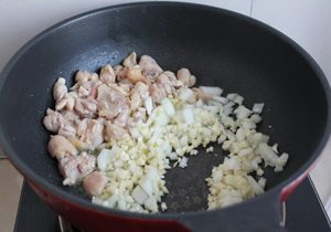 西班牙海鲜饭,炒好的鸡腿肉拨到一边，放入洋葱和蒜末炒香。