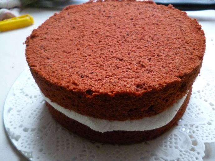 红丝绒裸蛋糕,切去蛋糕顶部凸起部分，翻转蛋糕体，拦腰一分为二（用牙签固定好位置，比较容易切分），在下半层蛋糕表面挤上满满的一层奶油，把上半层蛋糕叠放上去，再挤上满满一层奶油。