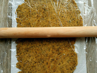 海苔全麦苏打饼,桌面铺上油纸，再放上发酵好的面团按扁，最后盖上保鲜膜，将面团擀成2mm左右厚的薄片。