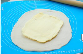 可颂,案板上撒少许高筋面粉，取出冷冻好的面团擀成比黄油大2倍的长方形面片，将擀开的黄油片放在面片中间。  （ 包黄油前，要保持黄油和面团的软 硬度相同）