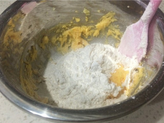 蛋黄纽扣小饼干,低筋粉和泡打粉混合均匀后，分次筛入，用硅胶刮刀翻拌混合