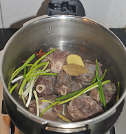 红焖牛尾,取高压锅，把牛尾倒入，注入清水600ml，加料酒、姜片、葱段、香叶、八角.