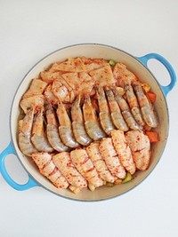 三汁焖锅,腌渍鸡翅、鱿鱼和大虾时放入的葱姜拣去不用，然后将鸡翅、鱿鱼和大虾铺在蔬菜丁上面，然后将味淋均匀的倒在食材上。