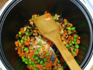 电饭锅什锦焖饭,继续放入胡萝卜、豌豆铲个半分钟左右，再撒点盐、鸡精拌匀。