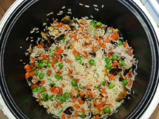 电饭锅什锦焖饭,倒入淘洗后的大米，用铲子把大米和蔬菜拌匀。