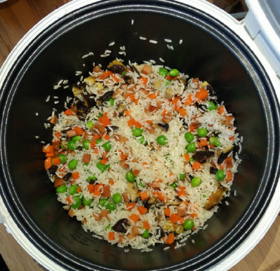 电饭锅什锦焖饭,倒入淘洗后的大米，用铲子把大米和蔬菜拌匀。