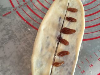豆沙花型排包,如图将包有豆沙的面团擀成长圆型，中间用刀切开（2头连着），在刀口一边摆放浸泡过的葡萄干若干粒；