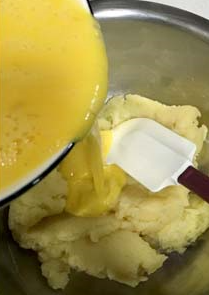 花环奶油泡芙,倒入盆中，分多次倒入打散的鸡蛋液，用软刮刀拌压