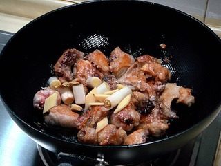 黄焖栗子鸡,完全把鸡块煎至金黄色后，放入腌鸡时用的葱姜香料等翻炒均匀。