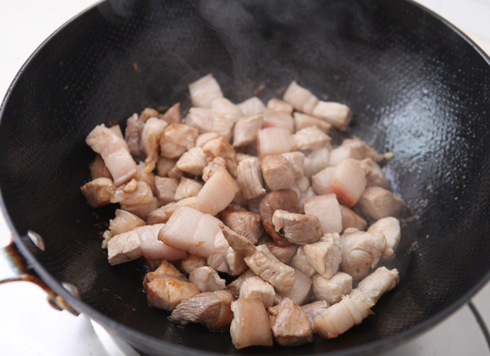 百叶结烧肉,将葱姜、五花肉块倒入锅中，快速翻炒让肉块裹上糖色。