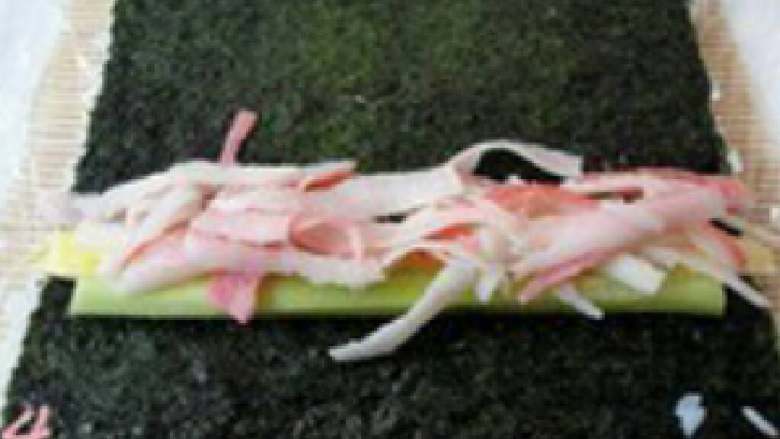 三文鱼寿司,将沾有米饭的海苔翻转放在竹帘上，当中放入黄瓜、鸡蛋皮、熟蟹肉，顺一边卷起卷紧。（海苔在里面）