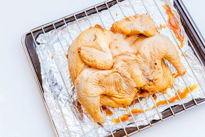 烤鸡,取出腌制好的鸡，放在烤架上，底下放烤盘并在下方铺一层锡纸（滴落的油脂不会直接弄脏烤盘，方便后续的清理工作）
