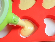 芒果酸奶冻芝士蛋糕,用手摸一下冷冻或冷藏后的酸奶糊，如果不黏手了即可分装芒果糊。将芒果糊用裱花笔分装到心形模具中。