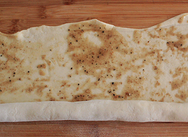 自制椒盐芝麻烧饼,在面皮上均匀的刷上步骤3调好的油酥，将面皮卷成卷。（可以一边卷一边抻面皮，这样做出的烧饼层多）