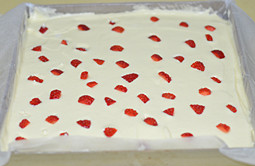 草莓蛋糕卷,将面糊倒入到铺了油纸的烤盘中，表面抹平后撒切成小粒的草莓粒。