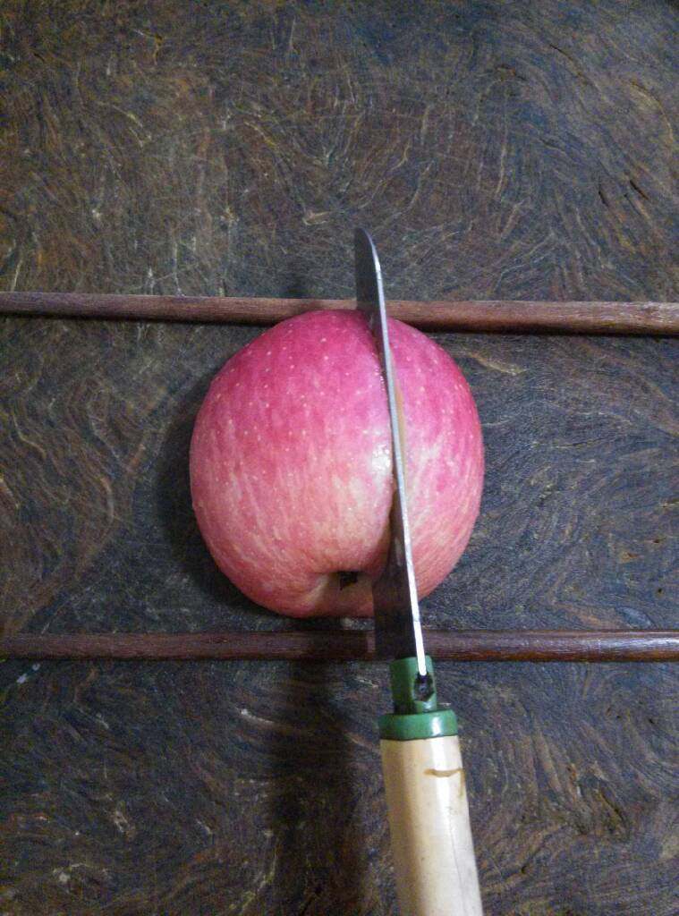 创意苹果，火龙果,取两粒苹果籽备用，把一半苹果放在筷子中间，距中垂线1厘米左右垂直切下，(火龙果也一样)