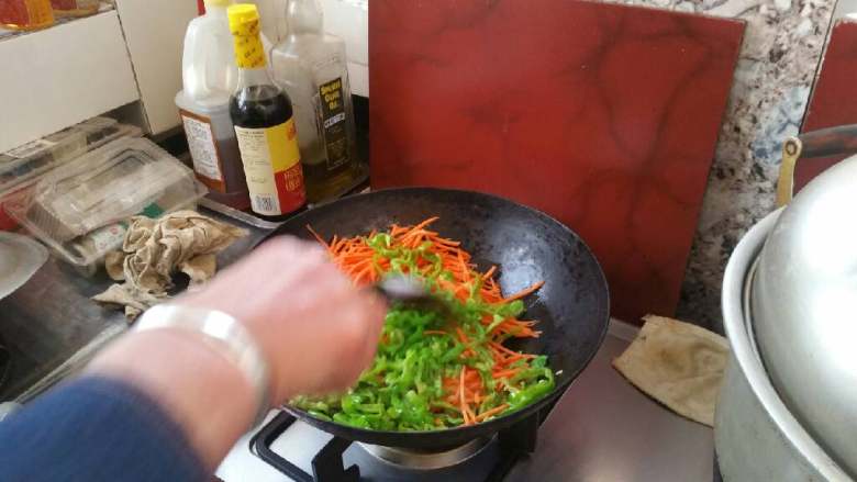 家庭鱼香鸡丝,锅中放油烧热，放入胡萝卜丝，青椒丝，煸炒片刻。