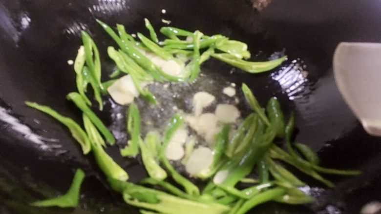 尖椒炒茶树菇#健康美颜餐#,锅里放入适量油，烧热后放入蒜片炒香，加入尖椒翻炒断生。