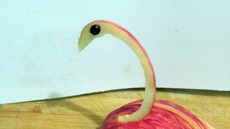 天鹅苹果拼盘,鹅头的适当位置斜插一刀，取一粒苹果籽放进去，另一边同样，这是天鹅的眼睛