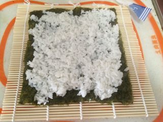 寿司,将海苔放在寿司卷帘上，铺上拌好的米饭并按压均匀。(不能太厚哦)