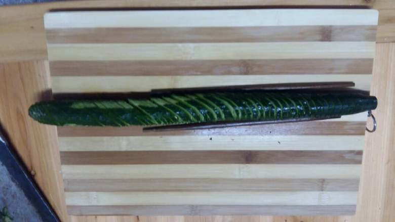 蓑衣黄瓜,用2根筷子垫在黄瓜底部，用斜切法均匀切好，因为下面有筷子垫着，可以大胆切，不会切断。
