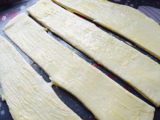 香浓炼乳面包.,黄油和炼乳拿出室温软化，拿出面团擀成长方形，分成四条，抹上融化的黄油炼乳酱，不要全抹完.