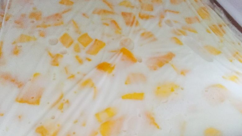 芒果椰汁糕,倒入容器里，下芒果粒，用保鲜纸包好放入冰箱冷冻30分钟左右.