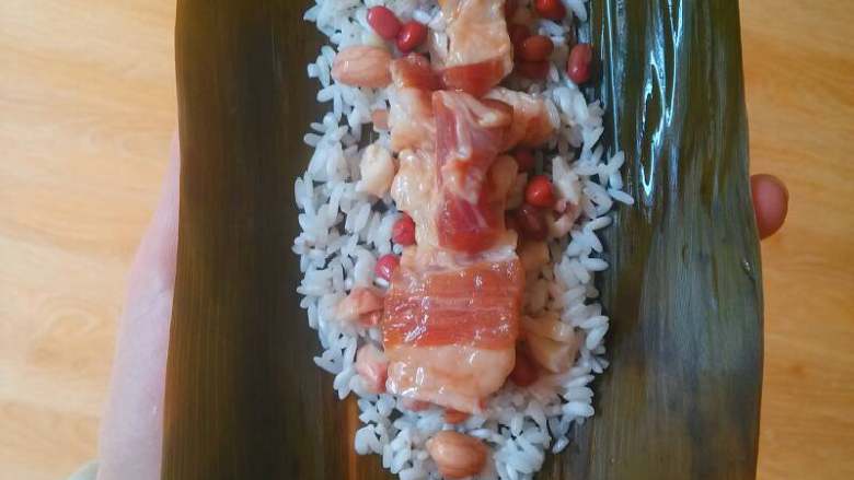 #端午节#粽情绽放,拿2张粽叶并排放平，放上大米摊成长形，均匀放上红豆，花生米，猪肉，再放入一层豆。