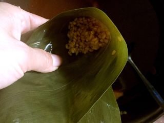 蛋黄猪肉粽,粽叶斜折呈漏斗状，放入少许糯米。用筷子插下，是糯米紧实。煮熟后粽尖会坚挺。