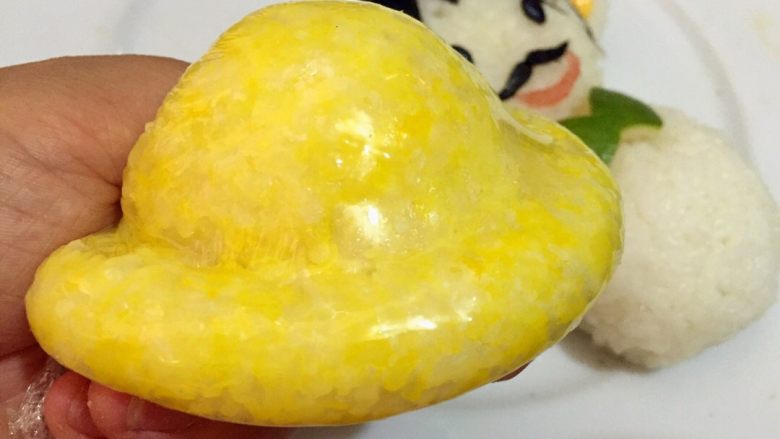 父爱如山,蒸好的南瓜和米饭搅拌均匀称为黄色饭团，取一块黄色饭团利用保鲜膜制作出帽子的形状
