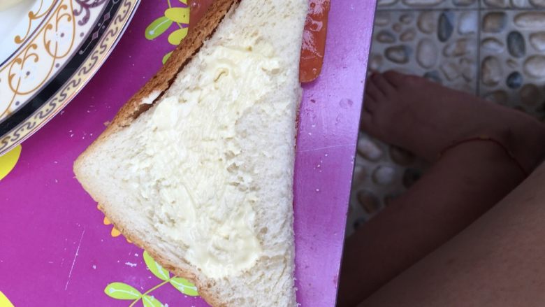 自制三明治,在拿一片盖在火腿片上，再在第二片面包片上涂抹沙拉酱
