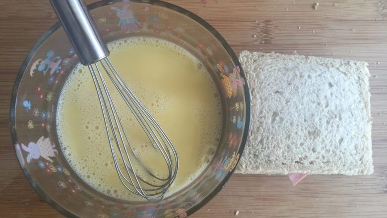 蛋奶西多士,把加入芝士火腿的完整三明治放入蛋碗里，让吐司表面裹上一层蛋液