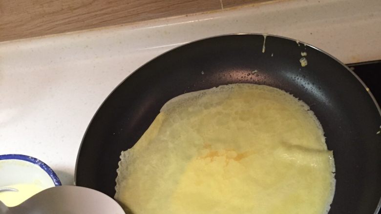 榴莲千层,舀一勺饼皮液，迅速让液体在锅内以流动的方式散开成饼皮状，用平滑的勺子从边上翻起饼皮，不要翻破了。