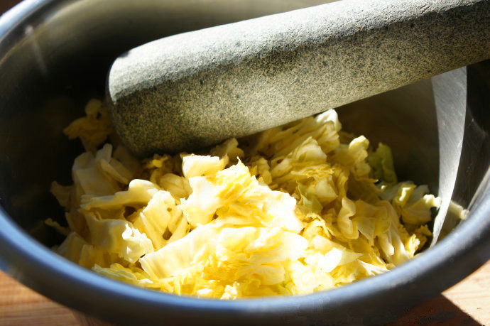 #夏天的味道#改善肠胃功能——神奇的益生菌德国泡菜,把卷心菜大致切碎，去掉硬的部分和菜心，加入海盐，乳清和 葛缕子籽，放入干净的大碗里，最好是不易碎的碗。用舂子捣打10分钟左右。十分钟后，菜汁出来，卷心菜的容量巨量减少。