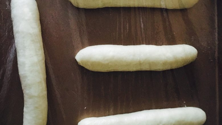 可爱的毛毛虫面包,将面包胚均匀摆放在烤盘上，盖保鲜膜入烤箱第二次发酵，需30-60分钟左右，至面包胚发酵至2倍大