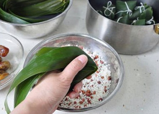 四角粽子的包法：红豆蜜枣粽子,将漏斗后面的苇叶盖在糯米上，然后用虎口处卡着抓住，一个四角粽子就基本定型了。