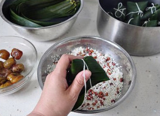 四角粽子的包法：红豆蜜枣粽子,将棉绳的一端用牙咬住，然后一手拿粽子，另一手拽着绳子缠紧扎结实即可。