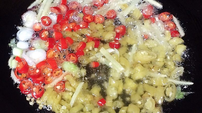 蒜苗爆炒章鱼足,锅中倒入适量油，加热后把生姜、红尖椒、小米椒下入锅内爆香。