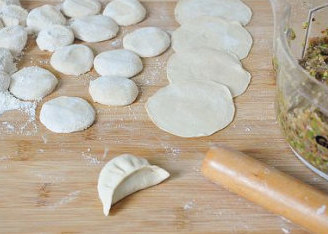羊肉芦笋香菇饺子,拿起饺子皮，将其卡在手的虎口处让它自然形成对折，然后将边缘依次折合捏紧即可。