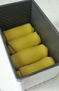 多汁熟粉南瓜面包 ,将面卷按照模具的宽度大小整好后放入土司盒。