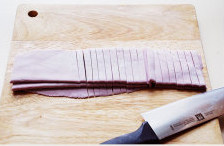 【紫薯手擀面】,将松弛好的面团撒上手粉，擀成大约2mm厚的面皮，在表面撒手粉，来回折叠，用刀切条；