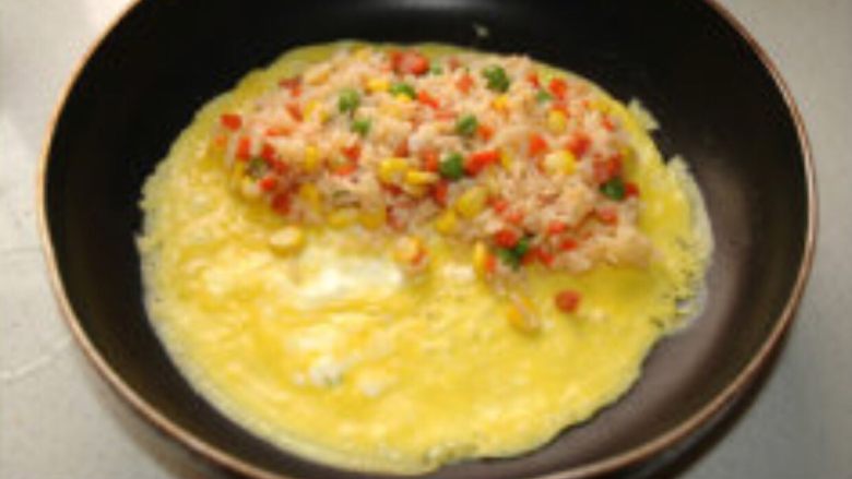 简易蛋包饭#挑战鸡蛋的100种做法#,在蛋液即将凝固时，将炒好的米饭倒在蛋皮的一侧。