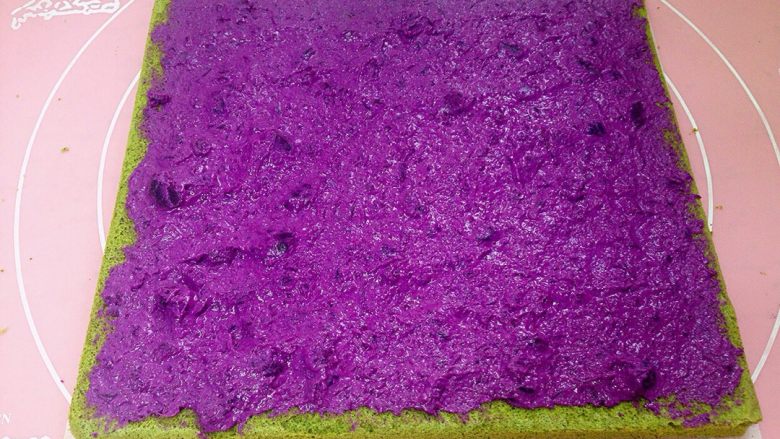 香芋布丁紫薯抹茶蛋糕卷,蛋糕远离自己的一边用刀斜切出45度斜边。把紫薯糊均匀地涂抹在蛋糕上面。