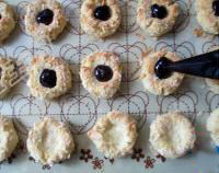 蓝莓杏仁软曲奇,取出烤箱，用裱花袋装入蓝莓酱，挤入饼干坯的窝里。最后在每个蓝莓酱上放上一颗新鲜蓝莓。再次入烤箱烤5分钟，至饼干表面金黄取出晾凉。